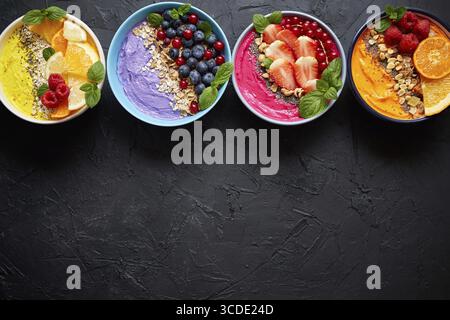 Divers smoothies frais sains colorés ou yaourts dans des bols. Avec fraises, kiwi, chia, mûres. Différents types de granola, flocons et noix Banque D'Images