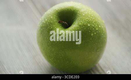 Closeup shot of green apple humide placé sur fond de bois clair Banque D'Images