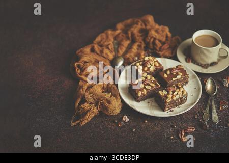 Les morceaux carrés de délicieux gâteau au caramel aux arachides et aux noix du brésil servis avec du café au lait, sur fond rustique. Avec espace de copie, pose à plat Banque D'Images