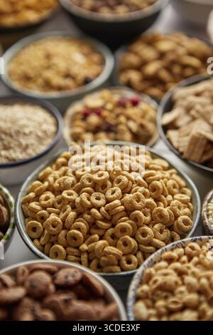 Gros plan et mise au point sélective. Composition de différentes sortes de céréales placées dans des bols en céramique avec des flocons de maïs, granola, céréales et flocons d'avoine. Pose à plat, Banque D'Images