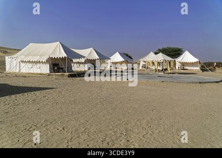 Village de tentes touristiques dans le désert du Thar, devant un bus rouge, près de Jaisalmer, Rajasthan, Inde du Nord, tentes blanches dans un paysage désertique sec sous un cle Banque D'Images