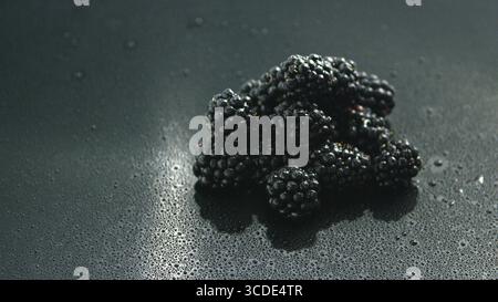Petit tas de mûres brillant frais allongé sur une surface en verre brillant humide dans l'eau gouttes Banque D'Images