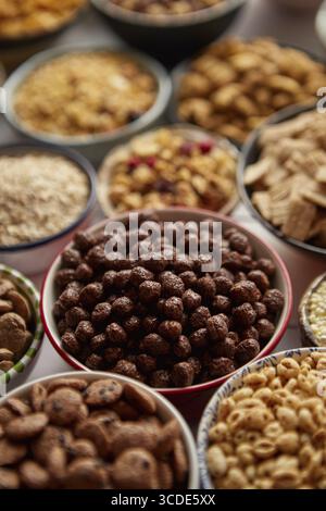 Gros plan et mise au point sélective. Composition de différentes sortes de céréales placées dans des bols en céramique avec des flocons de maïs, granola, céréales et flocons d'avoine. Pose à plat, Banque D'Images
