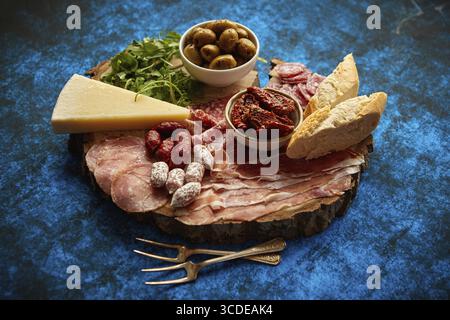 Délicieux mélange de différentes collations et hors-d'œuvre. Tapas espagnoles ou antipasti italiens sur une assiette en bois. Vue de dessus. Placé sur la table bleue Banque D'Images
