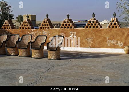 Village de tentes touristiques dans le désert du Thar, près de Jaisalmer, Rajasthan, Inde du Nord, cour traditionnellement peinte avec des chaises devant un mur de briques Banque D'Images