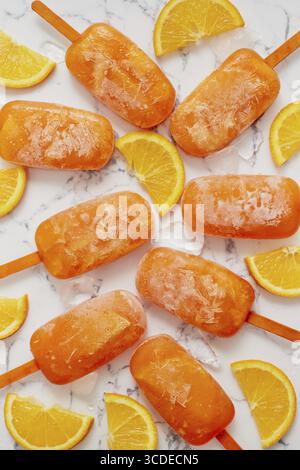 Popsicles surgelées faites maison avec des oranges fraîches oragniques placées avec des glaçons sur une table en marbre. Plat, vue de dessus Banque D'Images