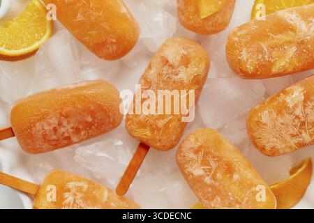Popsicles surgelées faites maison avec des oranges fraîches oragniques placées avec des glaçons sur une table en marbre. Plat, vue de dessus Banque D'Images