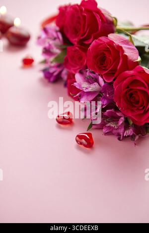 Bouquet de fleurs mixtes avec des roses, des bougies et de l'acrylique en forme de coeur décorations sur fond rose. Cadeau pour la Saint-Valentin, le 8 mars ou date romantique. Banque D'Images