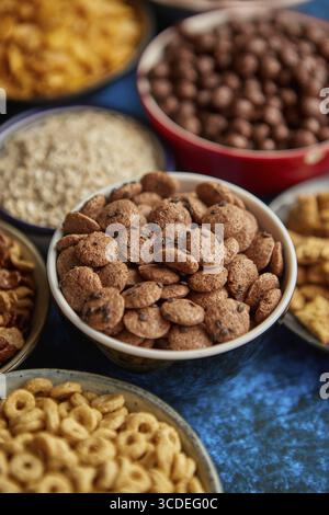 Assortiment de céréales de différentes sortes placées dans des bols en céramique avec des flocons de maïs, granola, céréales et flocons d'avoine. Flat lay, vue de dessus sur la table rouillée bleue avec Banque D'Images