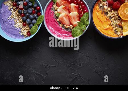 Divers smoothies frais sains colorés ou yaourts dans des bols. Avec fraises, kiwi, chia, mûres. Différents types de granola, flocons et noix Banque D'Images