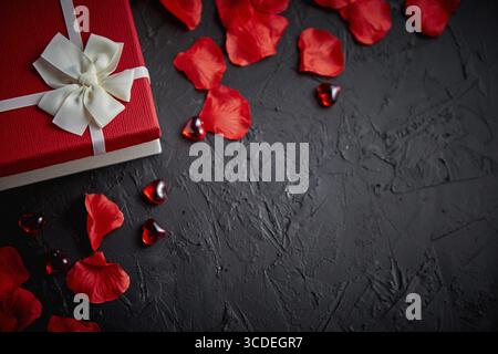 Boîte-cadeau sur noir table de pierre. Maison de vacances romantique douce arrière-plan avec des pétales de rose, décoration en forme de coeur en acrylique. Valentines Day background. Haut de la vie Banque D'Images