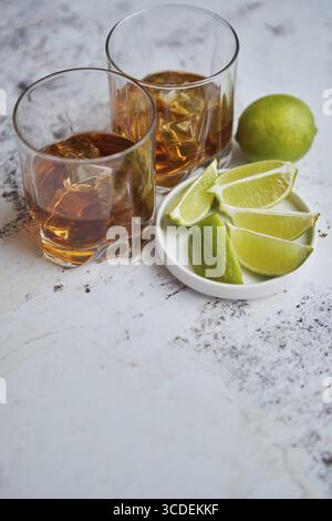 Boisson aigre de whisky avec citron vert dans le verre sur fond rustique de pierre. Deux verres remplis de glace et de chaux Banque D'Images