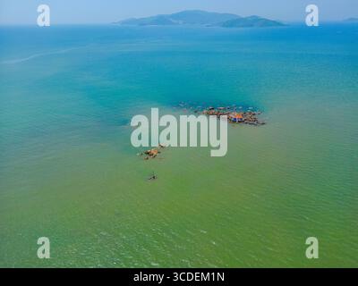 Vue aérienne du petit îlot rocheux avec des eaux turquoise et des îles montagneuses lointaines près de Nha Trang, Vietnam Banque D'Images
