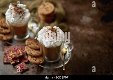 Deux grands verres avec chocolat chaud, crème fouettée et cannelle en poudre sur le dessus. Servi avec des biscuits au beurre au chocolat. Concept de dessert sucré Banque D'Images