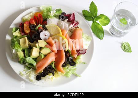 Salade avec saumon fumé, avocat, olives, citron, laitue et légumes frais sur une assiette blanche. Nourriture saine. Directement au-dessus. Banque D'Images