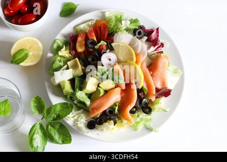 Salade avec saumon fumé, avocat, olives, citron, laitue et légumes frais sur une assiette blanche. Nourriture saine. Directement au-dessus. Banque D'Images