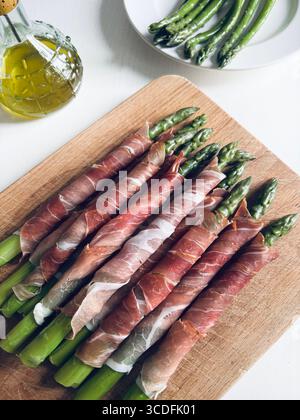 Jeunes asperges fraîches enveloppées de viande de prosciutto dans une planche à découper en bois. Directement au-dessus. Banque D'Images