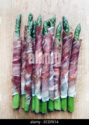 Jeunes asperges fraîches enveloppées dans de la viande de prosciutto sur un fond en bois. Directement au-dessus. Banque D'Images