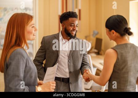 Homme d'affaires souriant et accueillant des professionnelles féminines avec poignée de main avant une session de planification collaborative. Banque D'Images