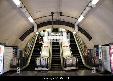 Panneau Way Out sur le métro londonien avec escalator en arrière-plan, symbolisant la sortie, la direction du voyage et le design emblématique des transports britanniques. Banque D'Images