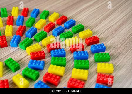 Blocs de construction en plastique coloré disposés dans un motif circulaire sur une surface en bois. Banque D'Images