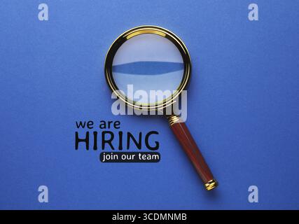Nous embauchons, rejoignez notre équipe. Inscription et loupe sur fond bleu, vue de dessus Banque D'Images