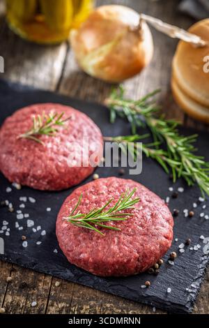 Patties de bœuf burger crues sur une planche à découper sur une table en bois. Banque D'Images