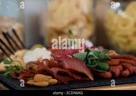 Une vue rapprochée présente une planche de charcuterie élégamment agencée avec prosciutto, salami, divers fromages, amandes et herbes fraîches, convient pour Banque D'Images