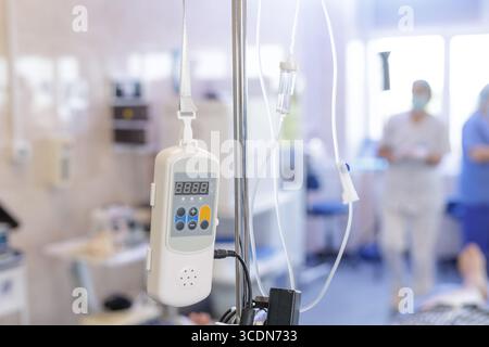 Faites un gros plan sur la pompe à perfusion et la ligne IV sur un poteau dans un service hospitalier lumineux, avec le personnel et le patient hors de propos, le traitement médical et la récupération Banque D'Images