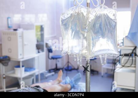 Poches de perfusion intraveineuse sur un support dans un service hospitalier lumineux avec un patient inconcentré transportant le traitement de récupération et des soins de santé professionnels Banque D'Images