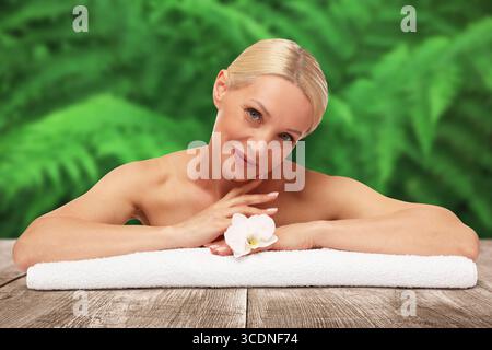 Belle femme se relaxant sur la surface en bois sur fond vert flou. Centre thermal Banque D'Images