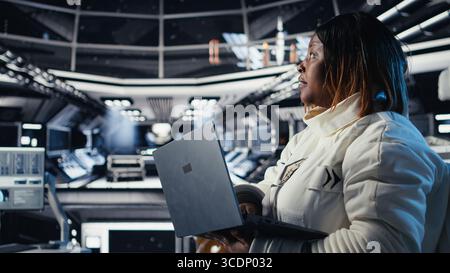 Astronaute revenant de la surface de la planète enlevant le casque, parlant avec un collègue à l'aide d'un ordinateur portable pour vérifier les paramètres. Cosmonaute finissant l'expédition en discutant avec un collègue mettant à jour le journal de vol Banque D'Images