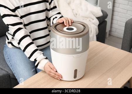 Jeune femme assise sur un canapé noir et allumant l'humidificateur moderne dans le salon, gros plan Banque D'Images