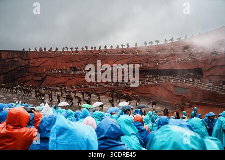 Lijiang, Chine - 24 octobre 2024 : le public vêtu d'imperméables colorés regarde le spectacle impression Lijiang avec des danseurs traditionnels sur les terrasses rouges de Jade Banque D'Images