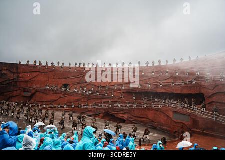 Lijiang, Chine - 24 octobre 2024 : le public vêtu d'imperméables colorés regarde le spectacle impression Lijiang avec des danseurs traditionnels sur les terrasses rouges de Jade Banque D'Images