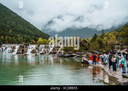 Lijiang, Chine - 24 octobre 2024 : les visiteurs en imperméables et parapluies se rassemblent au bord de l’eau pour admirer et photographier les cascades de Blue Moon Valley, Banque D'Images