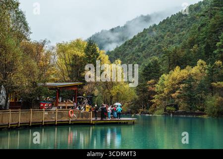 Lijiang, Chine - 24 octobre 2024 : les touristes se rassemblent sur une plate-forme d'observation en bois au-dessus des eaux turquoises, entourés d'arbres colorés dans Blue Moon Valley, L. Banque D'Images