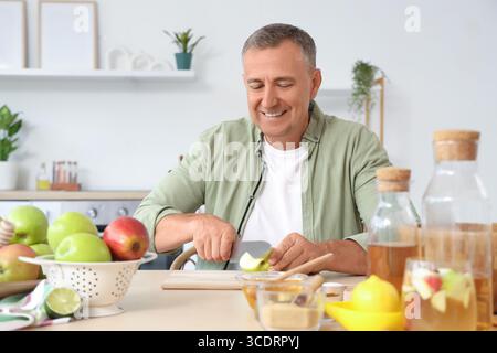 Homme mature coupant la pomme pour le cidre à table dans la cuisine Banque D'Images