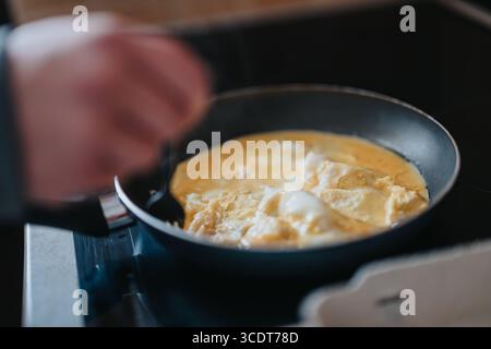 Gros plan de la préparation d'œufs brouillés dans une poêle sur une cuisinière, mettant en évidence la cuisson et l'activité culinaire Banque D'Images
