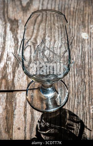 Verre à vin brisé avec des morceaux brisés sur une table en bois, sur un fond flou Banque D'Images