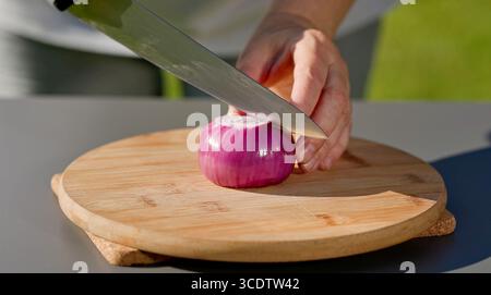 le chef coupe l'oignon rouge frais sur une planche à découper pour préparer un repas sain. cuisine extérieure, gros plan sur la nourriture Banque D'Images