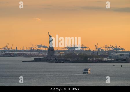 Vue de Lady Liberty se dresse haut contre le baiser ardent du coucher du soleil, sa silhouette un phare de liberté au milieu du port animé, , New York, New York Banque D'Images