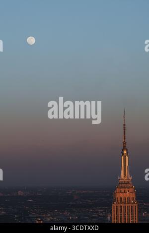 Vue de l'Empire State Building est baigné dans la lueur chaude du coucher du soleil, tandis que la lune est suspendue haut dans le ciel, New York, New York, États-Unis. Banque D'Images