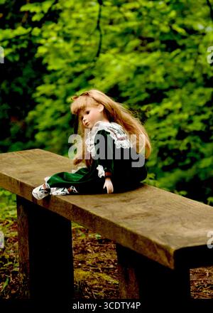 Une poupée portant une robe verte est assise sur un banc en bois devant un fond vert. Banque D'Images