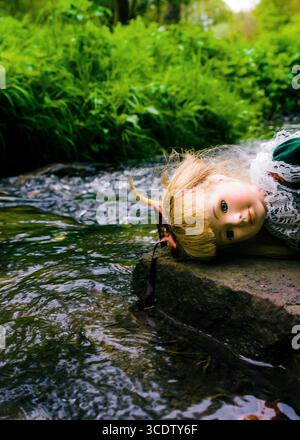 Une poupée repose sur un rocher à côté d'un ruisseau. Banque D'Images