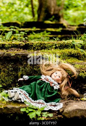 Une poupée vêtue d'une robe de velours vert repose sur une marche de pierre recouverte de mousse dans un cadre forestier. Banque D'Images