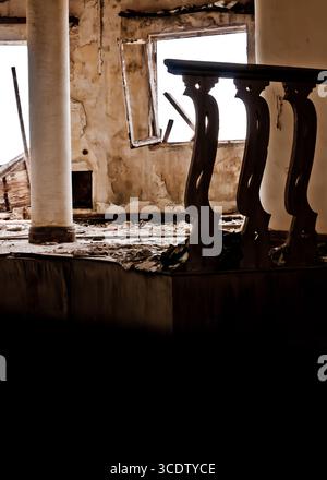 Une photo intérieure d'un bâtiment délabré, avec un pilier altéré, une balustrade décorative en bois et un cadre de fenêtre. Les murs montrent des signes de déc Banque D'Images