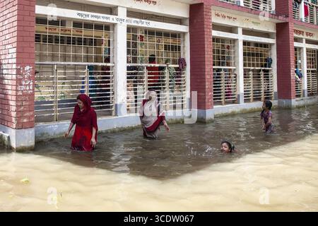 Noakhali, Bangladesh - 02 septembre 2024 : vue sur les eaux de crue engloutissant les bâtiments tandis que les résidents traversent, la brique rouge contrastant avec l'eau trouble. Banque D'Images