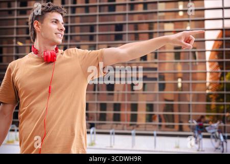 Jeune homme avec des écouteurs pointant sur le côté avec un sourire confiant Banque D'Images