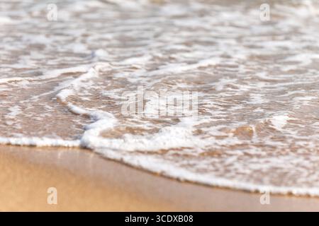 Douce vague d'océan bleu sur la plage de sable. Arrière-plan flou. Banque D'Images